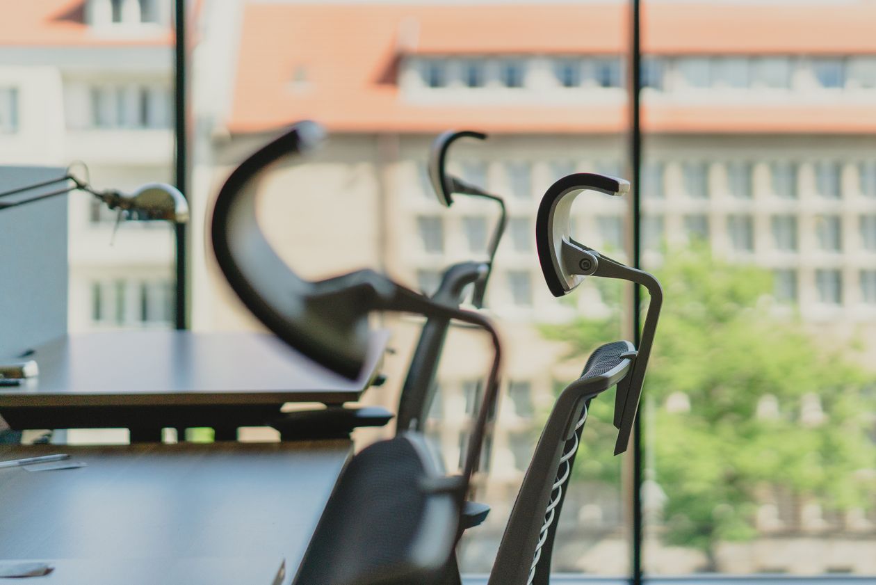Empty office chairs and desks beside large windows